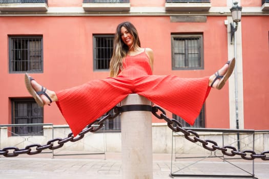 A vibrant and lively young woman confidently poses playfully on a chain barrier, exuding her unique blend of style and charisma against a colorful and captivating backdrop that enhances her look