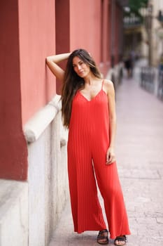 In a vibrant urban setting, a stylish woman in a flowing red jumpsuit poses elegantly, exuding charm and sophistication, attracting the admiration of curious onlookers who admire her fashion sense
