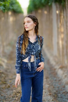 A stylish and fashionable young woman poses gracefully and elegantly amidst a serene and peaceful vinecovered pathway, showcasing her trendy and chic outfit with confidence and poise
