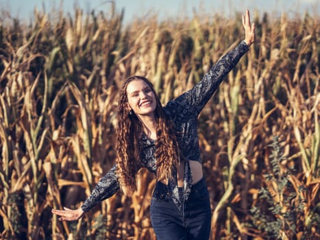 A cheerful young woman with lively curly hair dances joyfully and playfully in a sunlit cornfield, embodying the essence of freedom and pure happiness as she celebrates life in nature