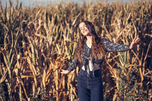 A joyful young woman delightfully poses amidst a lush, expansive cornfield, radiating pure happiness and a profound connection with the beauty of nature all around her on that sunny day