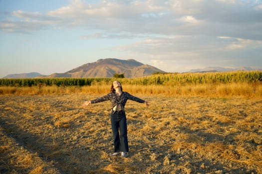 A person joyfully embraces freedom in a stunning golden field under a beautifully painted sky, with rolling hills as an idyllic backdrop, capturing the essence of nature and pure joy
