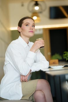 Vertical low angle view portrait of an elegant businesswoman drinking coffee in a cafeteria at night