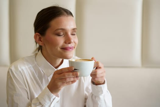 Beauty woman closing the eyes to enjoy the aroma and taste of a latte coffee in a modern cafeteria