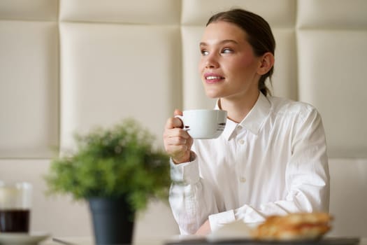 Elegant young businesswoman enjoying morning coffee looking away and dreaming in a coffee shop