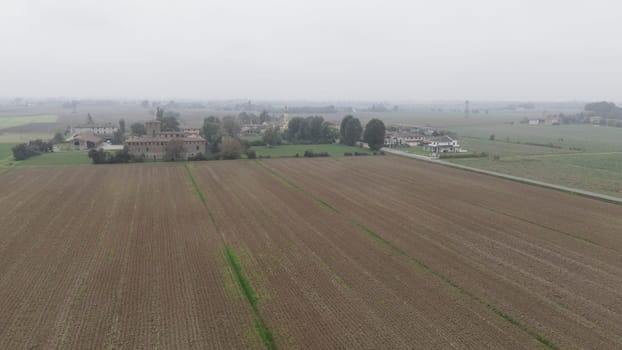 Piacenza, Italy October 15th 2024 An aerial view of cultivated fields and farmhouses in the italian countryside on a foggy day with the sky completely covered by clouds