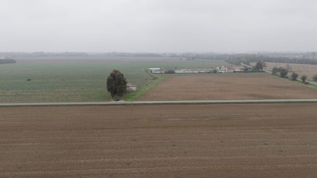 Piacenza, Italy October 15th 2024 A car is driving on an empty country road dividing two plowed fields in the italian countryside in autumn