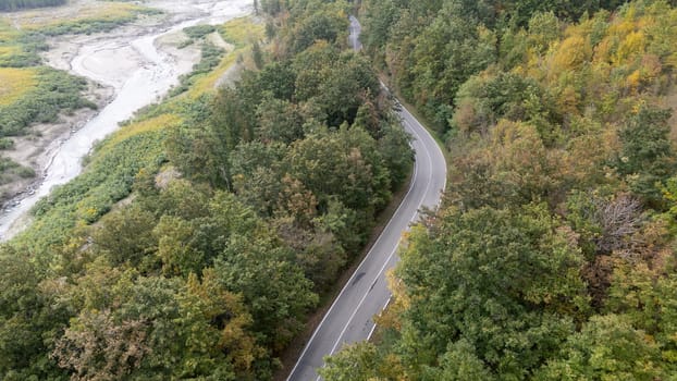 Aerial view of a winding road going through a forest next to a river in autumn. Lago di Mignano, Val Tolla, PC, Italy