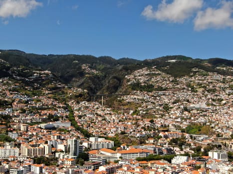 View of the city of Funchal, located among the mountains along the Atlantic coast, with traditional houses with red roofs. High quality photo