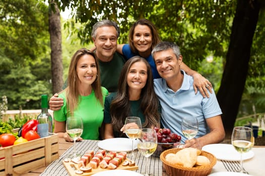 A group of five friends gathers around a table filled with wine and delicious food in a vibrant outdoor setting. Laughter and joy fill the air as they celebrate together.