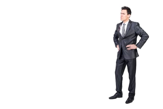 Full body of nervous and irritated male boss standing with hands on waist and looking at camera with frown face in studio against white background