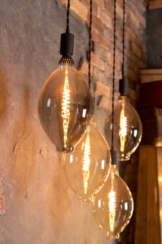 A group of four lighted lamps hanging from the ceiling. The lamps are all different sizes and shapes, but they all have a similar design. The lamps are lit up, creating a warm and inviting atmosphere