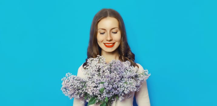Portrait of beautiful happy smiling woman with bouquet of fresh lilac flowers, wildflowers on blue background