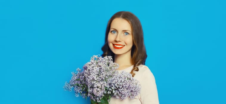 Portrait of beautiful happy smiling woman with bouquet of fresh lilac flowers, wildflowers on blue background