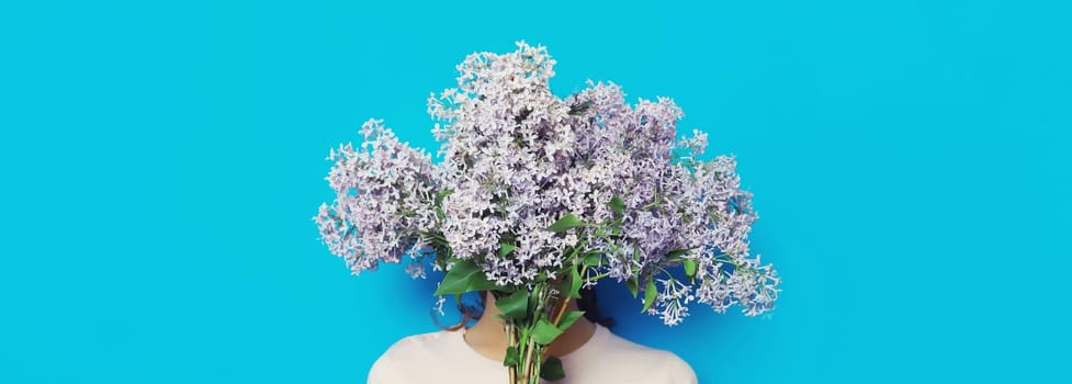 Portrait of woman covering her head with bouquet of fresh lilac flowers on blue background