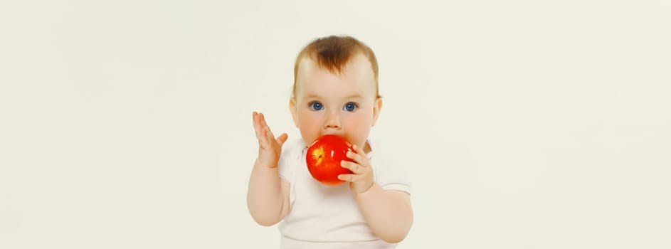 Portrait of cute baby eating red apple fruit sitting isolated on white studio background