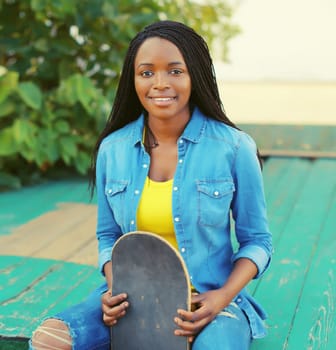 Portrait of happy smiling young african woman model posing with skateboard in the city
