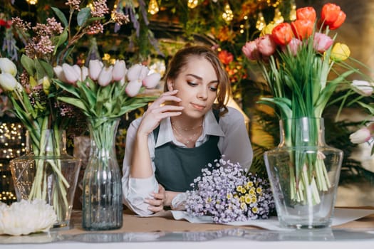 A woman in her florist shop collects bouquets of flowers. The concept of a small business. Bouquets of tulips for the holiday on March 8