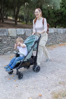 A woman is pushing a stroller with a child in it. The child is smiling and the woman is smiling as well. The scene is peaceful and happy