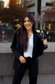 Portrait of cheerful young Hispanic businesswoman standing outdoors in bustling downtown area.