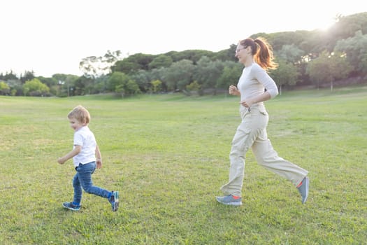 Mother and son are running on the grass in a park, enjoying a beautiful summer day together