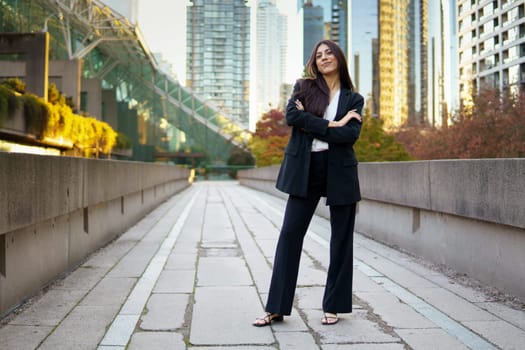Successful businesswoman standing outdoors in an urban city area with glass skyscrapers.