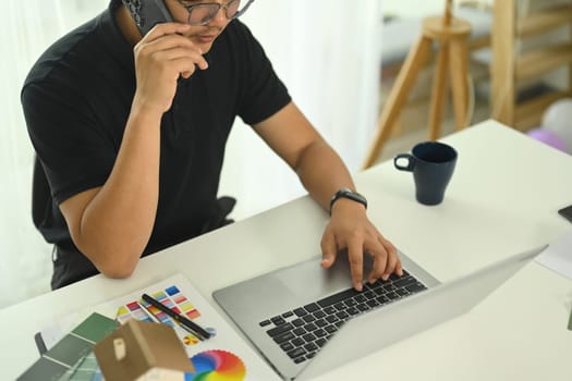 Interior designer talking on cell phone and using laptop at creative workplace.
