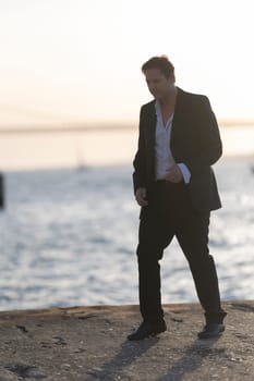Businessman is walking on a pier at sunset, enjoying the view and the fresh air