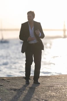 Elegant businessman is dancing by the water at sunset