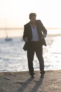 Businessman is happily dancing on a pier by the sea at sunset