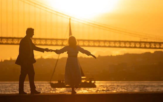 Silhouette of a couple holding hands and dancing by the river at sunset