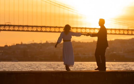 Man and a woman are dancing by the river at sunset