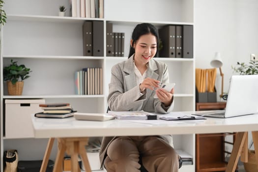 Beautiful businesswoman using mobile phone while sitting at modern office.