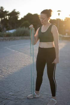 Athletic woman is exercising outdoors, using a resistance band for a biceps curl workout