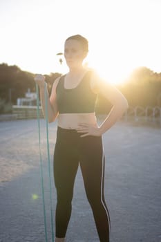 Sportswoman is working out with a resistance band outdoors at sunset
