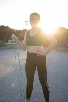 Young woman is exercising with an elastic band outdoors at sunset