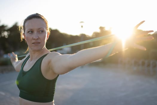 Sportswoman is exercising with a resistance band outdoors at sunset