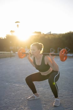 Young woman is weightlifting outdoors at sunset