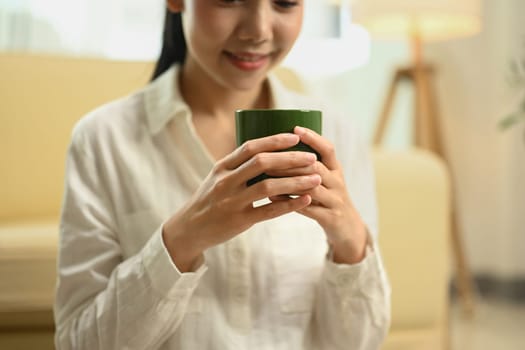 Cropped shot of happy young woman enjoying quiet moment with a warm drink in living room.