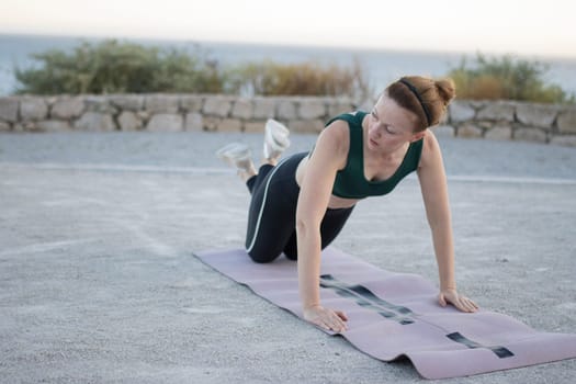 Woman is doing push-ups on a fitness mat near the sea