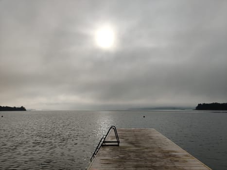 Relaxing foggy Northern summer scene with swimming platform, pontoon or Wooden pier with a steel ladder into a Baltic sea. Summer holiday vacation in Finland with beautiful sea