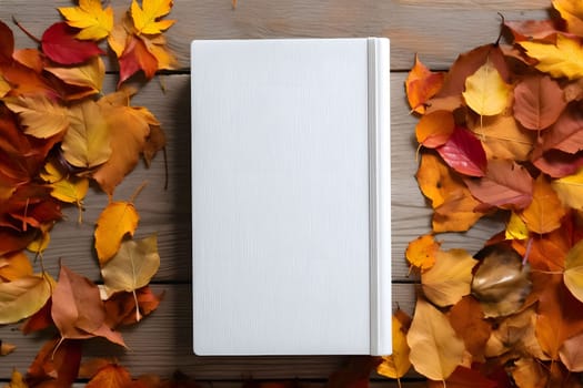 A blank notebook lying flat on a wooden surface, surrounded by colorful autumn leaves. The composition creates a simple, yet beautiful, still life with a warm and cozy atmosphere.