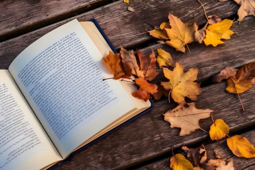 An open book rests on a wooden table with fallen autumn leaves scattered around. The image evokes a sense of tranquility and the beauty of nature