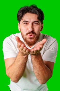 Young man blowing a kiss against a bright green background close up