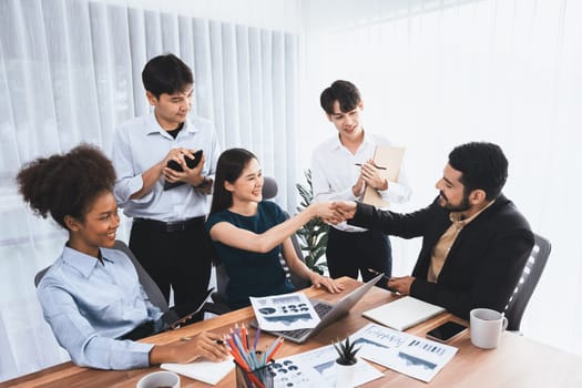 Diverse coworkers celebrate success with handshake and teamwork in corporate workplace. Multicultural team of happy professionals united in solidarity by handshaking in office. Concord