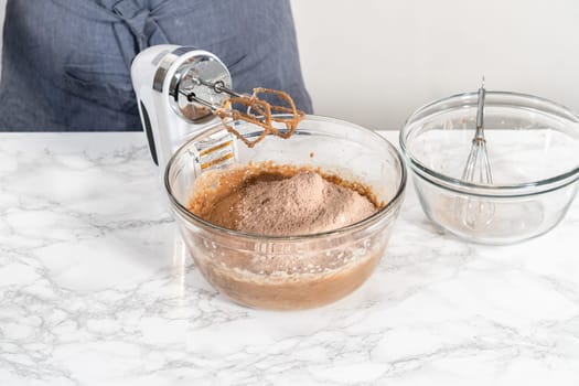 Mixing wet ingredients in a large glass mixing bowl to bake red velvet cupcakes with white chocolate ganache frosting.