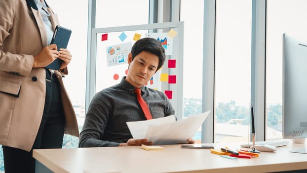 Two business people talk project strategy at office meeting room. Businessman discuss project planning with colleague at modern workplace while having conversation and advice on financial report. Jivy