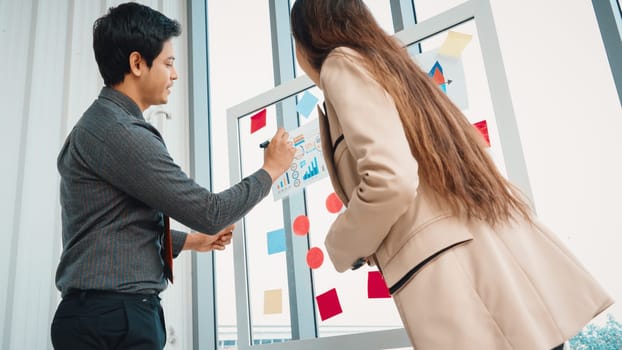 Business people work on project planning board in office and having conversation with coworker friend to analyze project development . They use sticky notes posted on glass to make it organized. Jivy