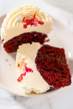 Sliced red velvet cupcakes with white chocolate ganache frosting on a white plate.