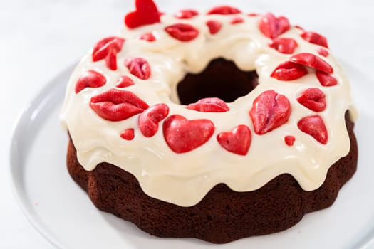 Freshly baked red velvet bundt cake with chocolate lips and hearts over cream cheese glaze for Valentine's Day.